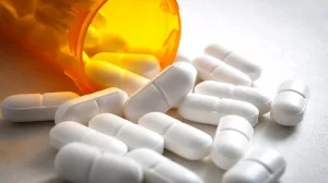 Nahaufnahme von orangefarbener Plastikdose, aus der Schmerztabletten herausfallen